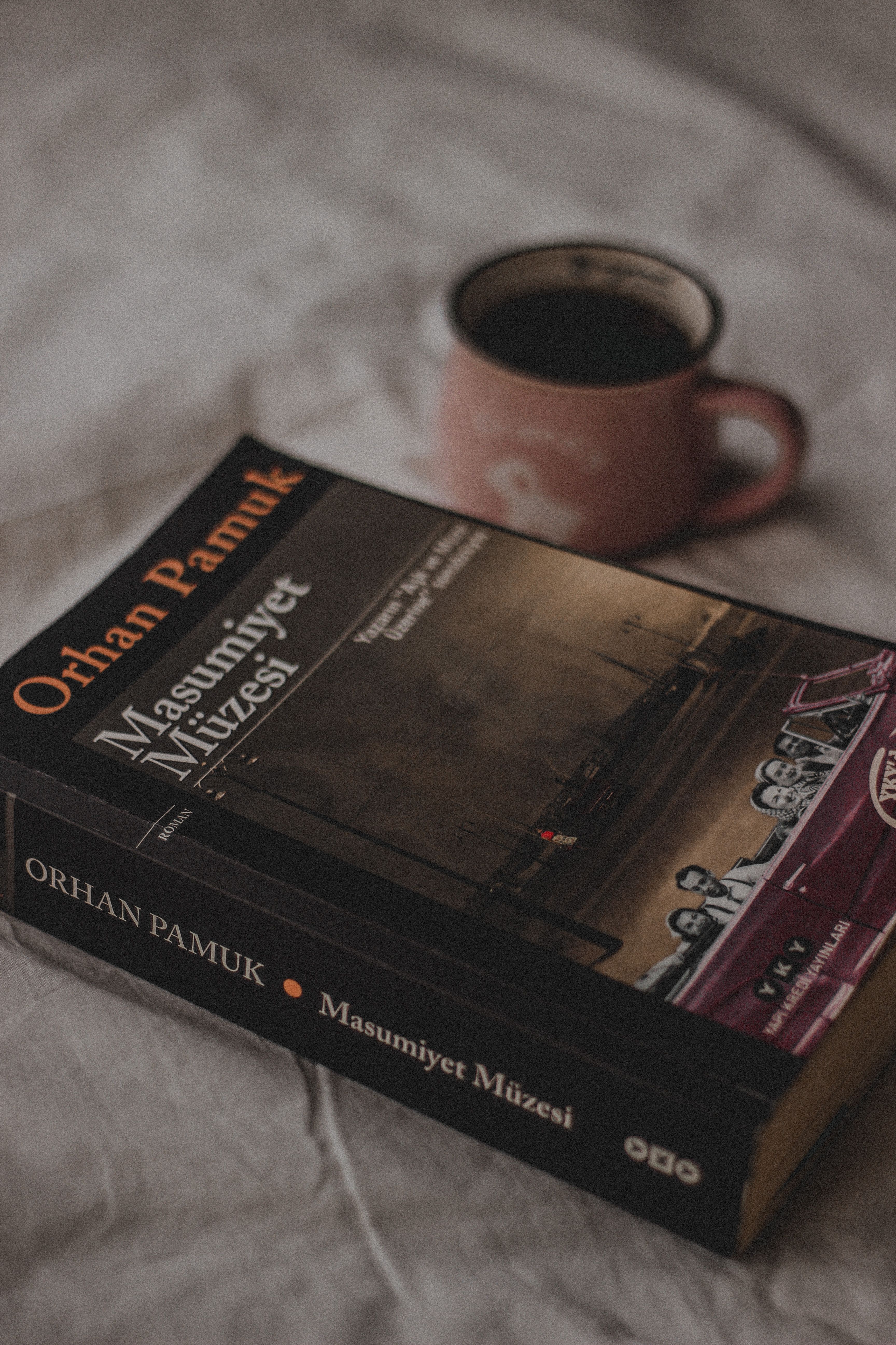 A close-up of Orhan Pamuk's book 'Masumiyet Müzesi' alongside a ceramic cup of coffee on a soft fabric.