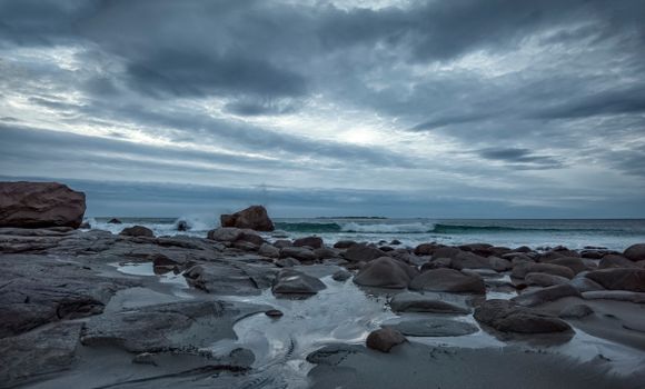 Moody view of rocky shore and cloudy sky at Nordland, Norway with waves crashing on rocks.