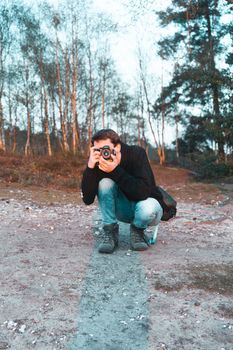 Man crouching and taking pictures in an outdoor wooded area during autumn. Ideal for nature photography themes.