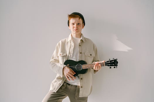 Young Man in White Crew Neck Shirt and Beige Dress Up Shirt  Holding Black Ukelele