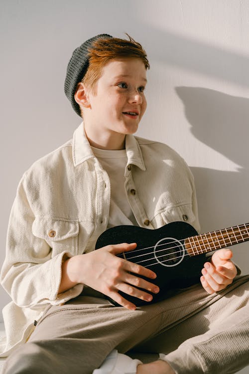 A boy wearing a face mask plays ukulele in front of a laptop Stock