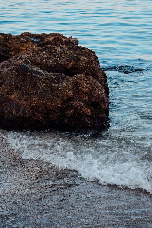 Free Serene image of waves gently crashing against a brown rock at the seashore, ideal for nature themes. Stock Photo