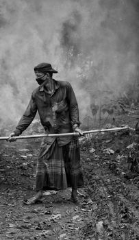 Black and white photo of a masked man standing with a stick outdoors in smoky surroundings. - Fotografer Sidoarjo