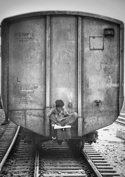 A Boy Sitting at the Rear of a Train Car on Railroad