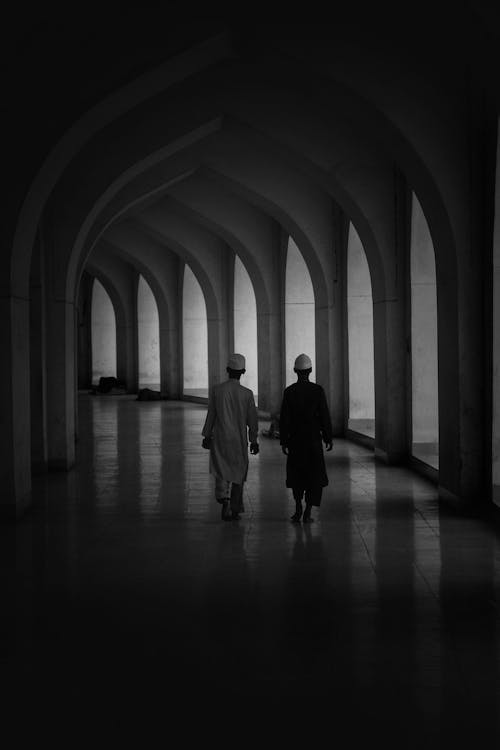 Free Monochrome Shot of Men Walking on an Arched Hallway Stock Photo