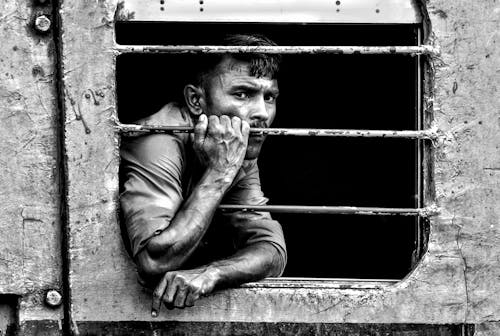 Grayscale Photo of a Man Holding onto a Grill