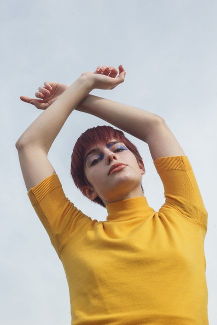 Low angle portrait of a woman with makeup in a yellow shirt against a clear sky.
