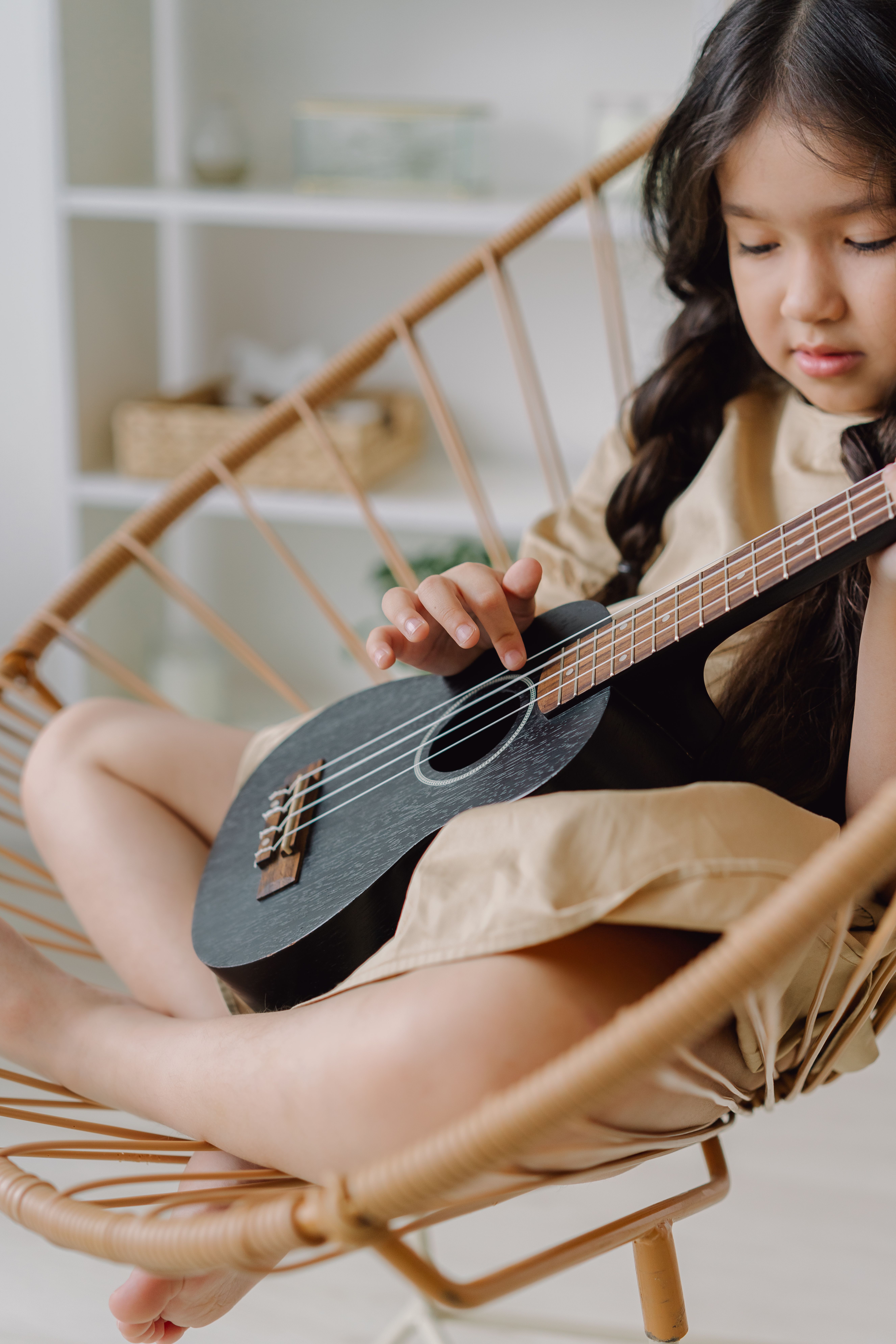 Young girl enjoying playing ukulele while sitting in a stylish rattan chair.