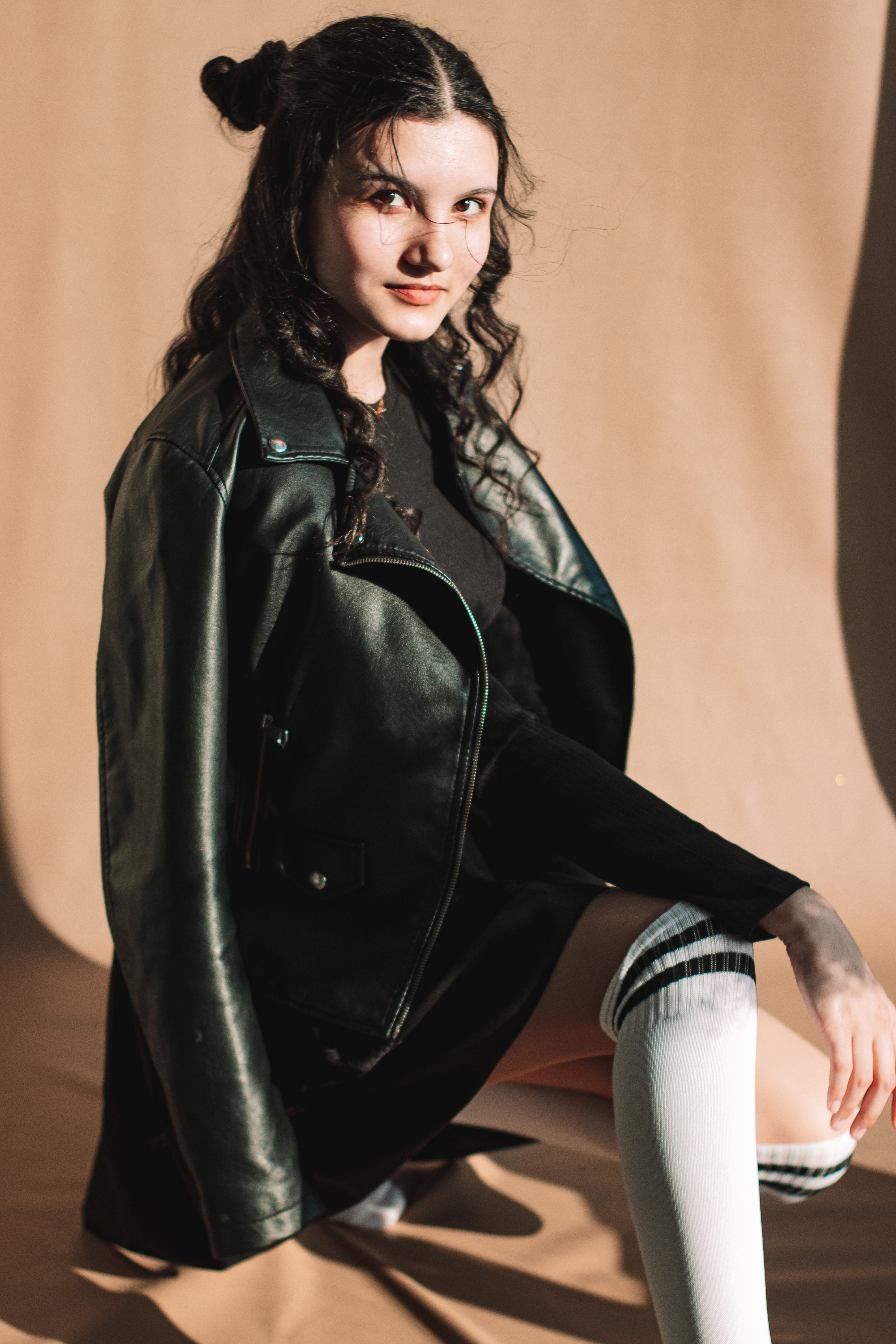 Stylish portrait of a woman in a leather jacket and knee-high socks, showcasing modern fashion.