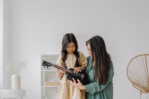 Photo of a Woman Teaching a Girl How to Play a Ukulele