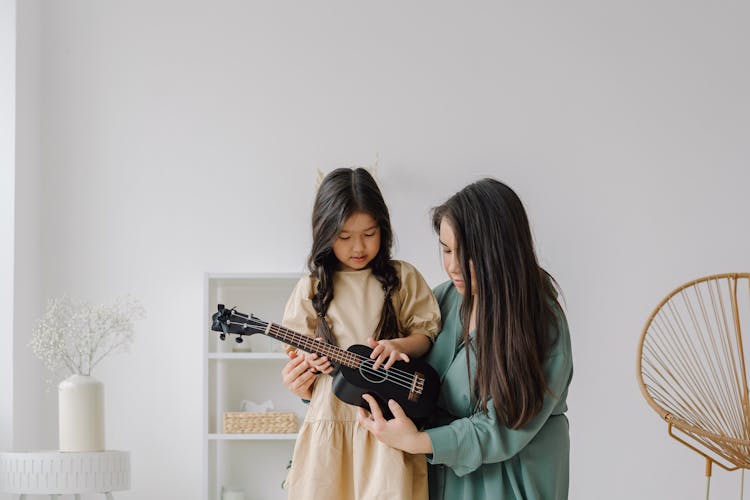 Photo Of A Woman Teaching A Girl How To Play A Ukulele