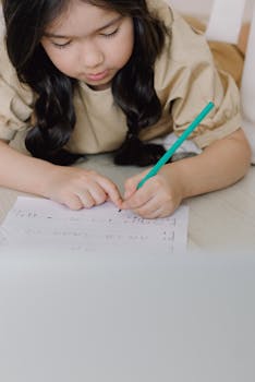 A young girl lying on the floor writing on a music sheet with a pencil indoors.