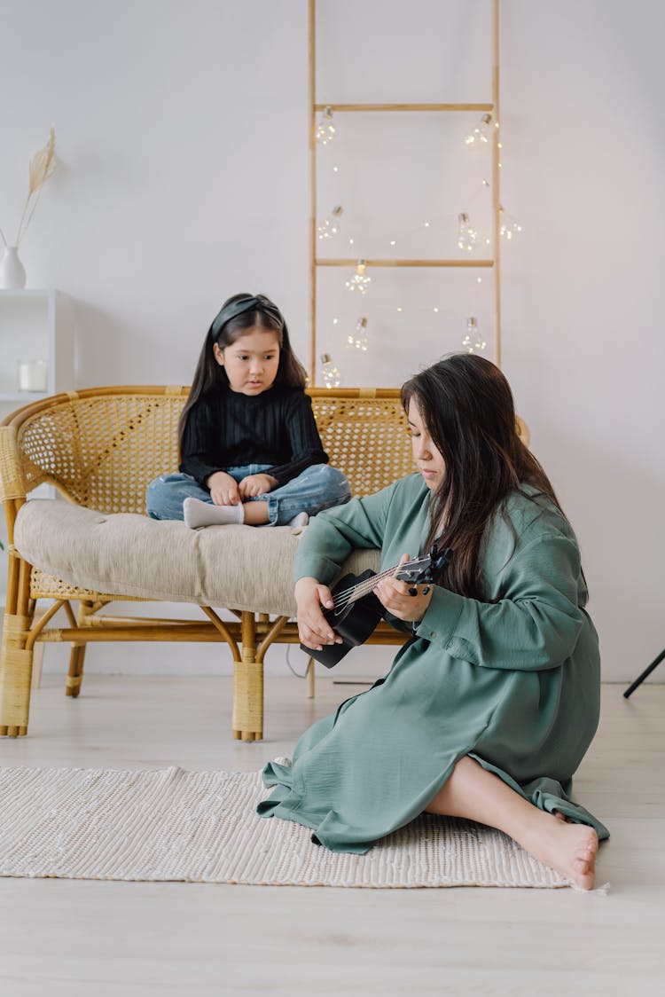 Girl Sitting On A Wicker Chair Watching A Woman Play The Ukelele