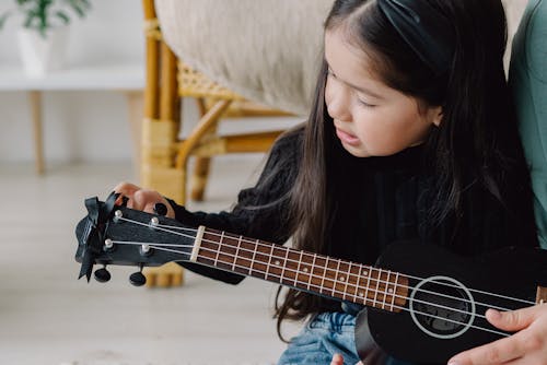 Girl in Black Long Sleeve Shirt Tuning a Ukelele