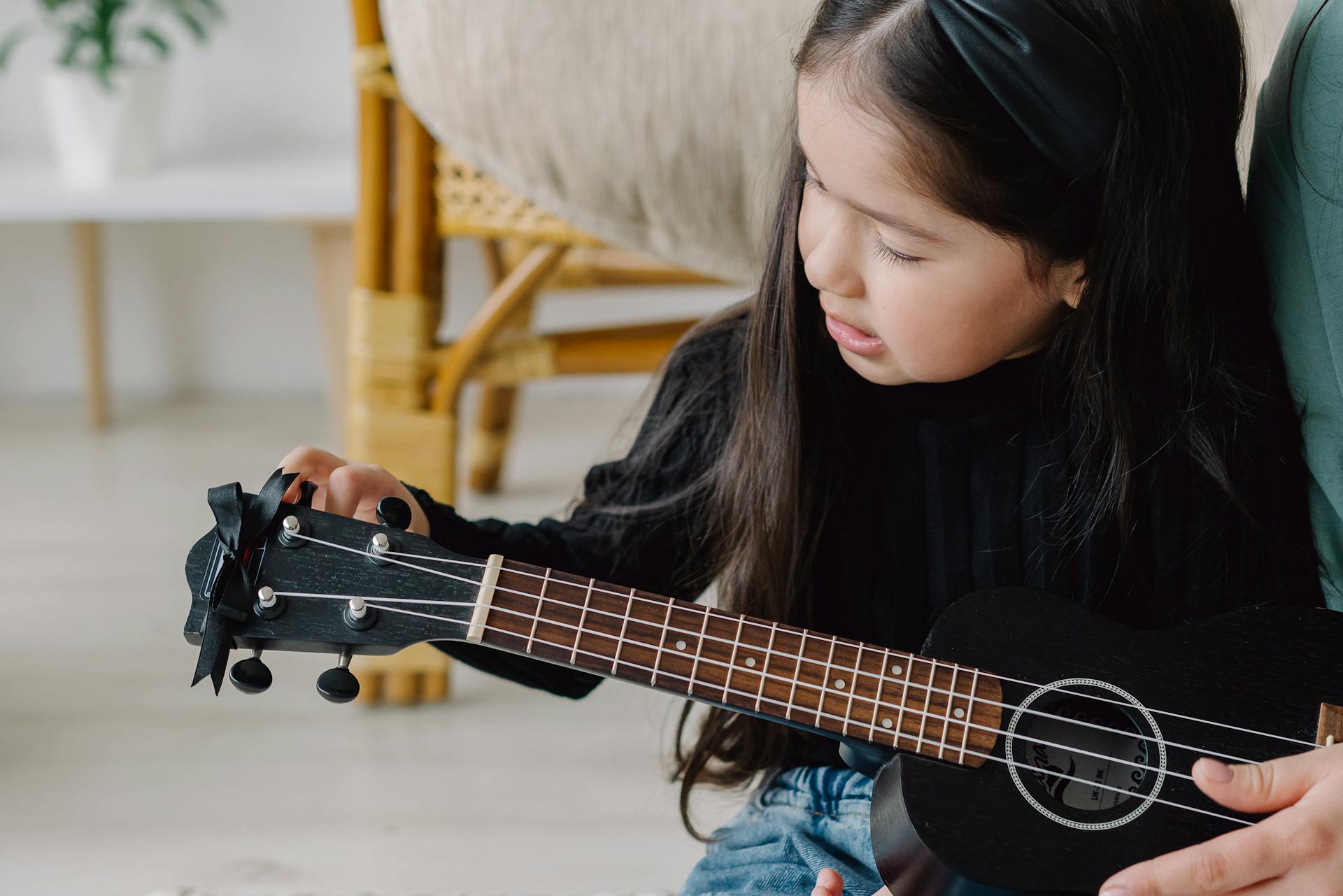 A young girl learns to play the ukulele, focusing on tuning the instrument, creating a peaceful home learning moment.