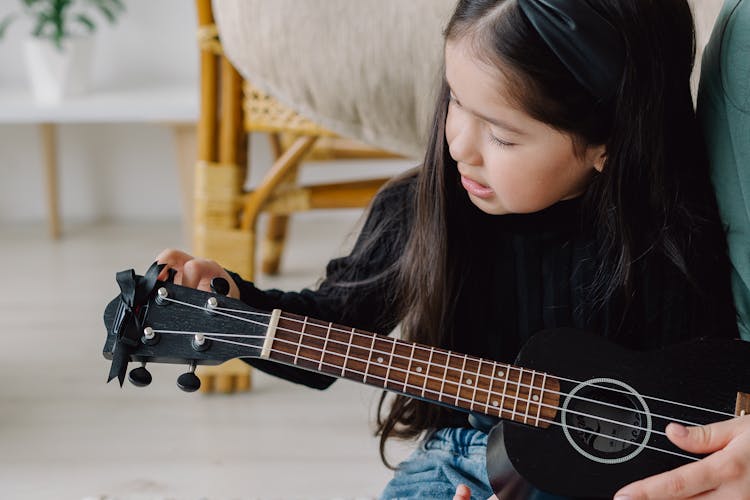 Girl In Black Long Sleeve Shirt Tuning A Ukelele