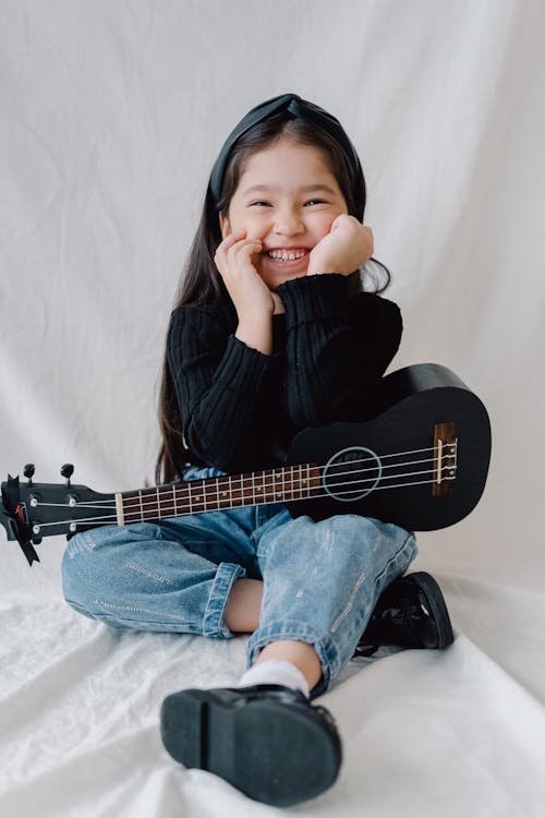 Girl in Black Long Sleeve Shirt and Blue Denim Jeans Sitting on White Fur Textile