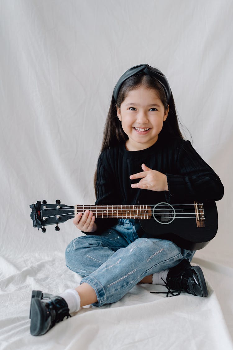 Girl In Black Long Sleeve Shirt And Denim Jeans Holding Ukulele