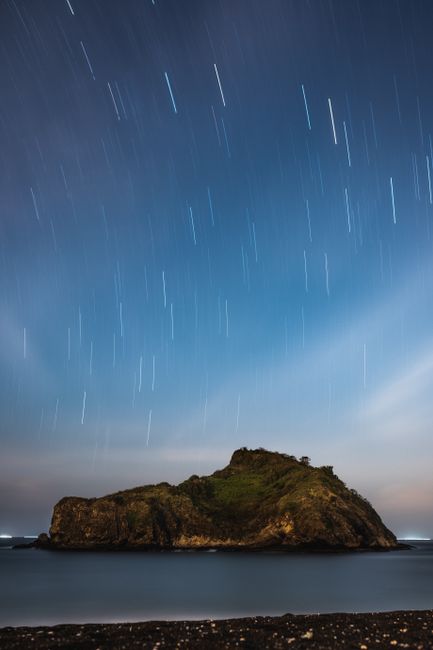 A mesmerizing view of star trails over a small islet in Indonesia's serene sea at night.