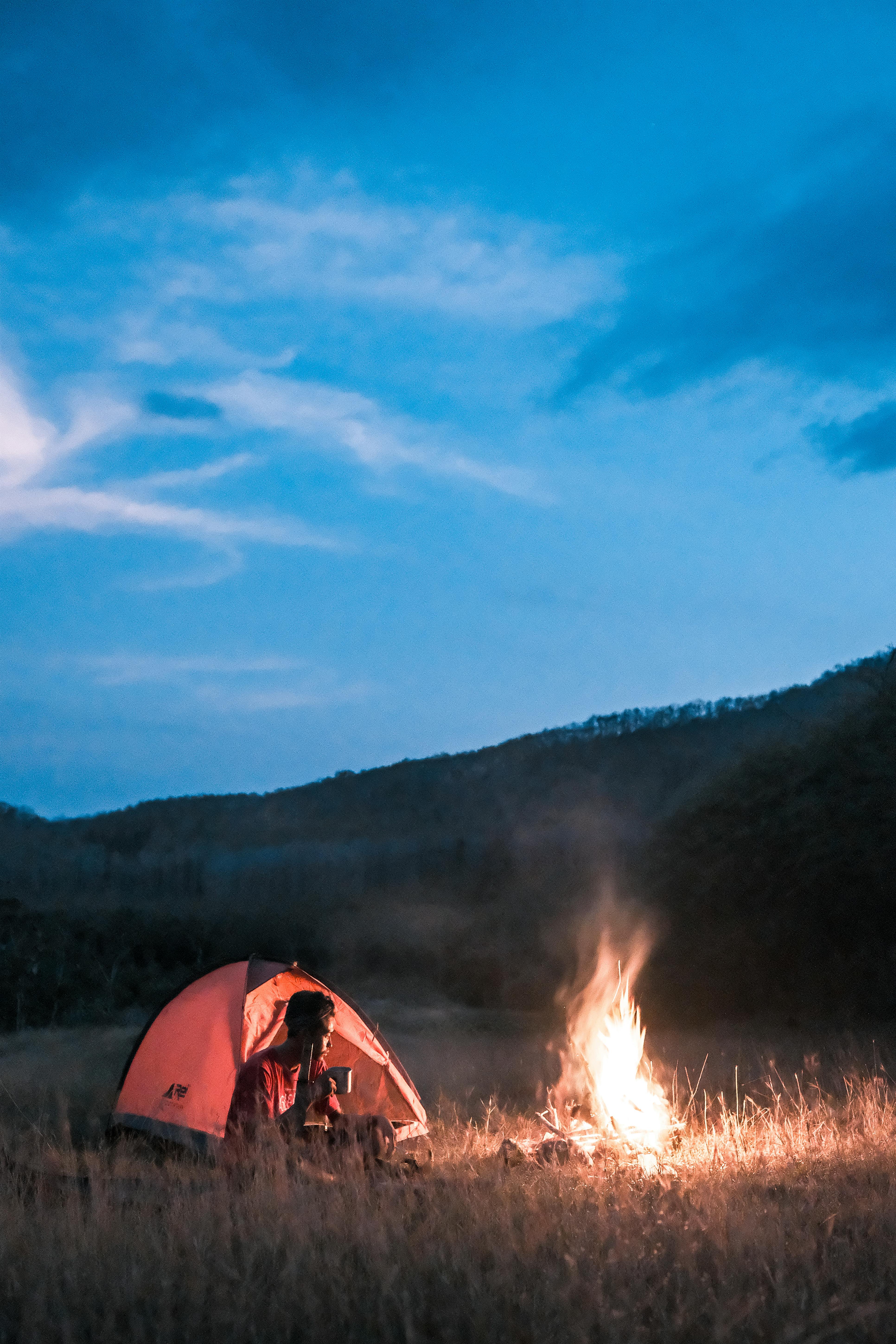 photo of a man sitting beside a campfire