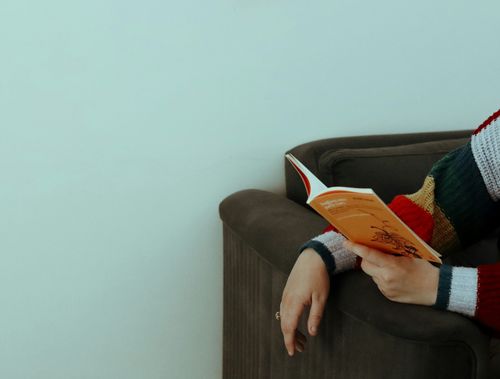Free Crop unrecognizable female in striped warm sweater studying fascinating book in gray soft sofa on white background Stock Photo
