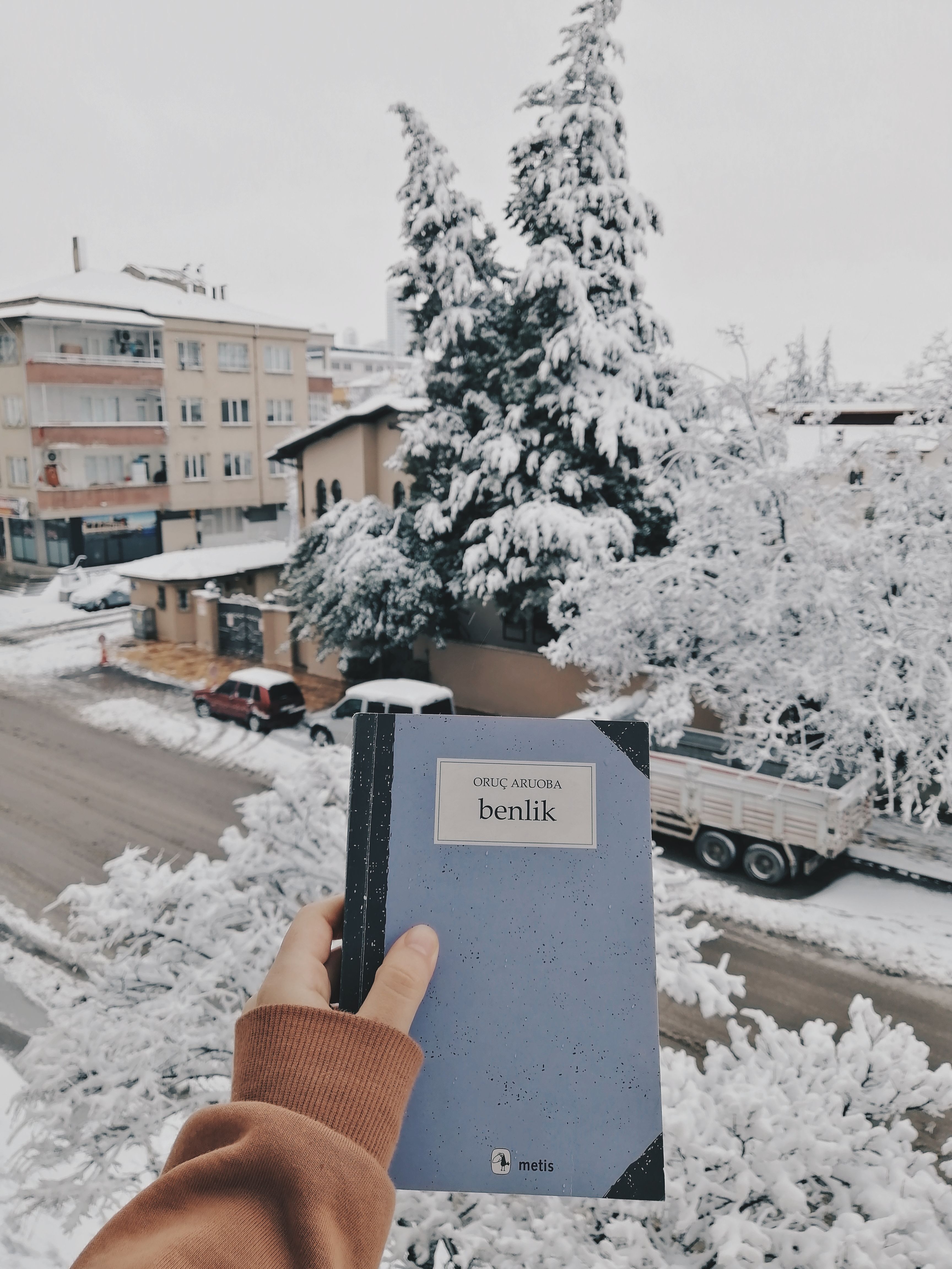 Hand holding a notebook with a snowy cityscape background, highlighting winter season ambiance.