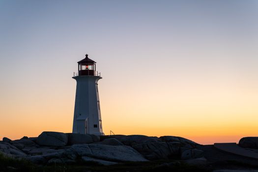 Peggy's Cove lighthouse stands silhouetted against a vibrant sunset sky in Nova Scotia, Canada.