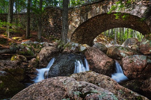 Aged stone footbridge over waterfall streaming through stones in woods