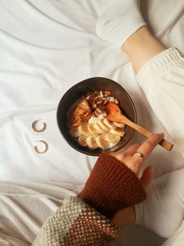 Warm and cozy breakfast in bed with banana slices, nuts, and wooden spoon in a bowl.
