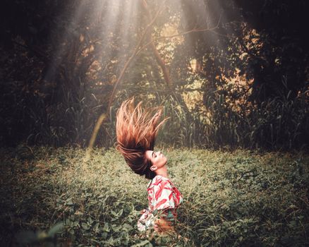 Woman in a tropical forest flipping her hair under rays of sunlight, creating a dynamic and natural scene.