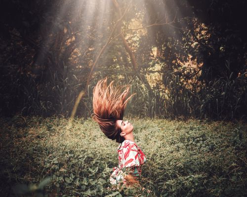 Free Woman in a tropical forest flipping her hair under rays of sunlight, creating a dynamic and natural scene. Stock Photo