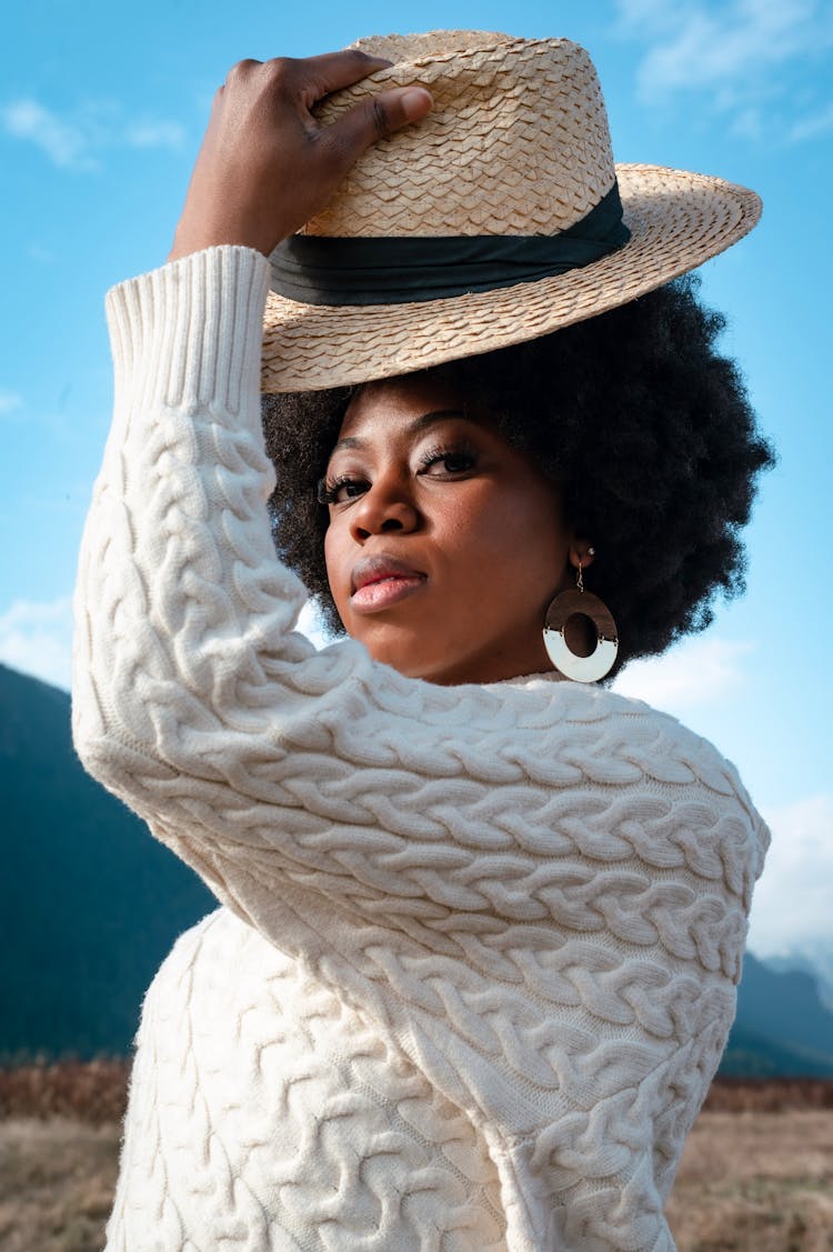 Woman In A White Sweater Looking At The Camera While Putting On Her Hat