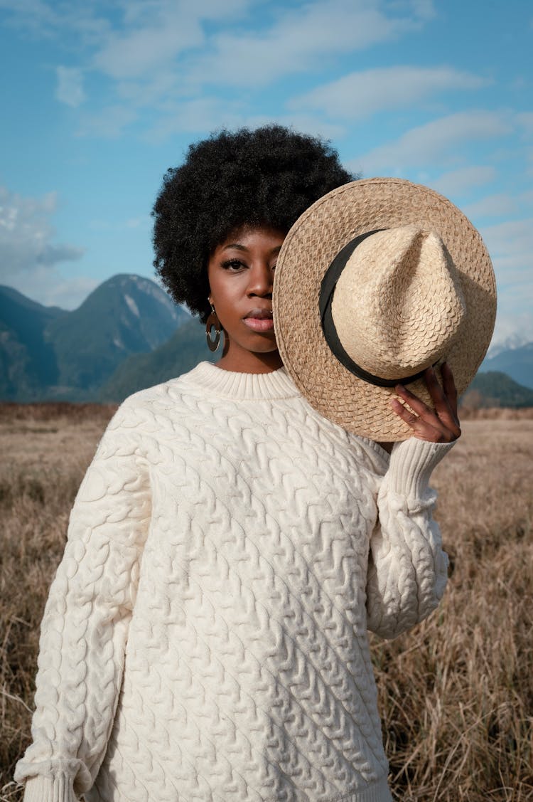 Woman With An Afro Hairstyle Holding A Hat Near Her Face