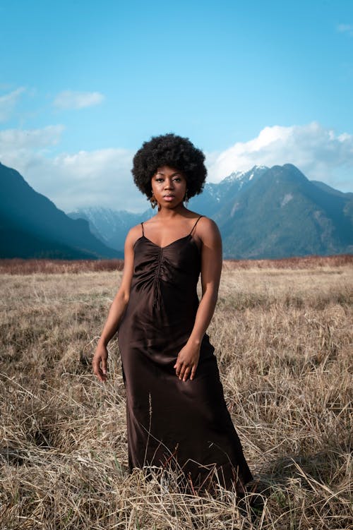 Photo of a Woman in a Black Dress Posing on Grassland