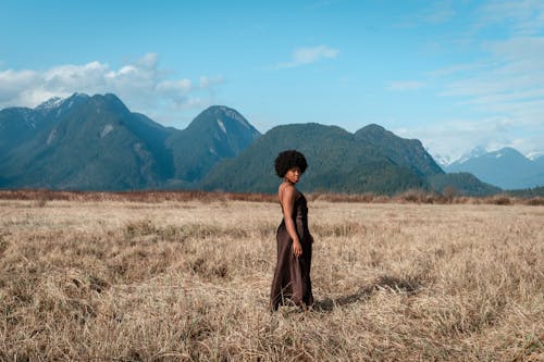 A Woman in Brown Dress Standing on Brown Grass Field