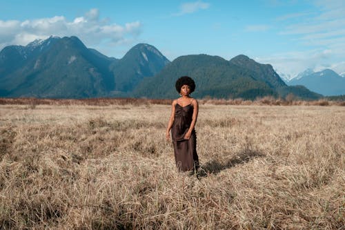 A Woman in Brown Dress Standing on Brown Grass Field