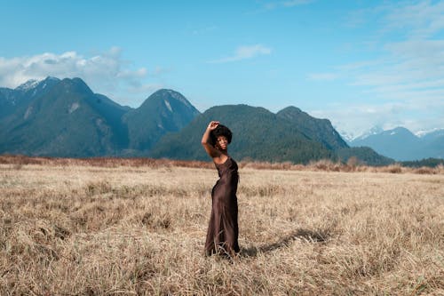 A Woman in Brown Dress Standing on Brown Grass Field