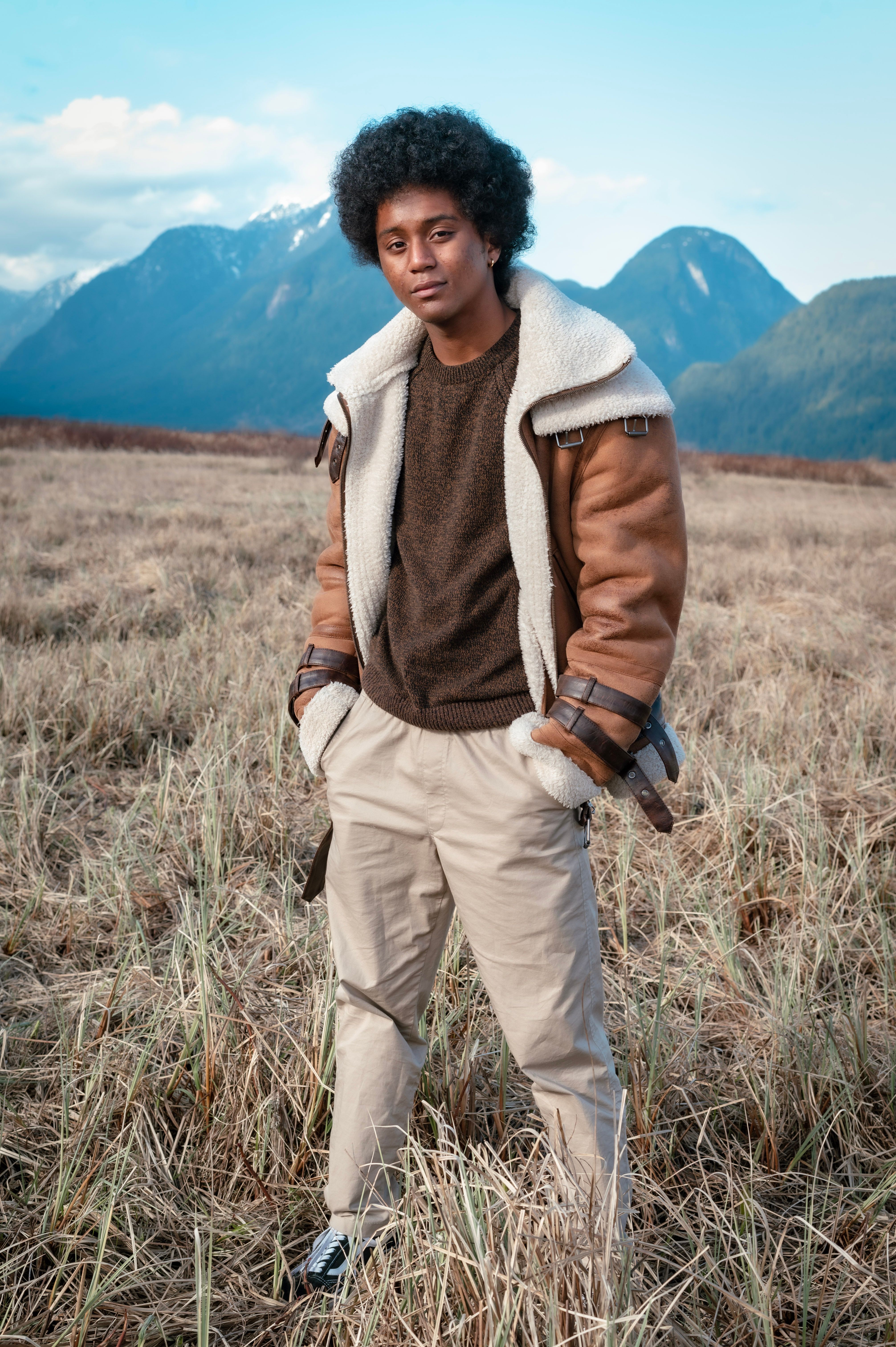 Stylish man posing in a rustic field with mountains in the background.