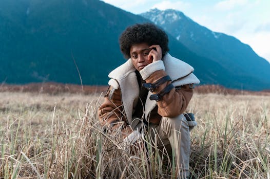 A fashionable man in a bohemian jacket poses thoughtfully in a picturesque mountain landscape.