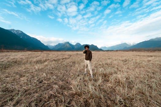 A person in a grassy field with majestic mountains under a blue sky.