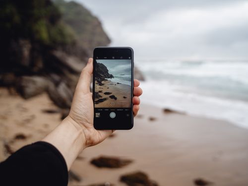 Free Hand holding smartphone capturing Stanwell Park's rocky beach. Outdoor photography at its best. Stock Photo