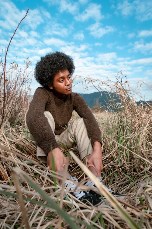 Man in Brown Sweater Sitting on Grass Field