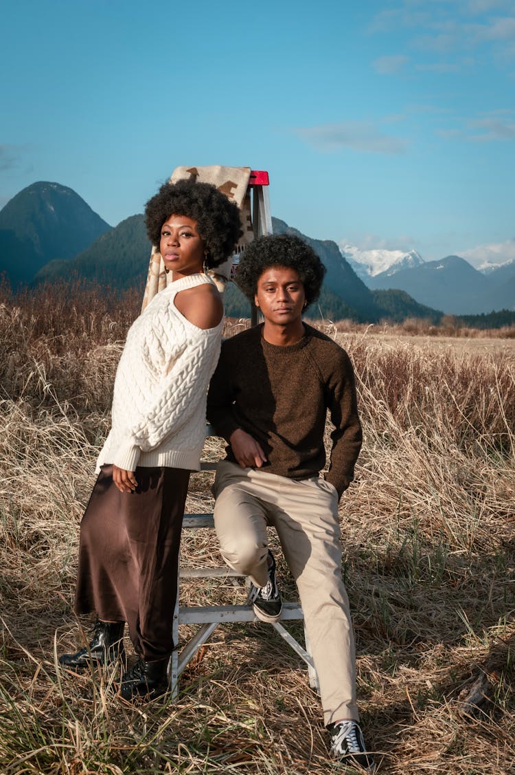 A Man And A Woman Sitting On A Ladder In The Grass Fie;d