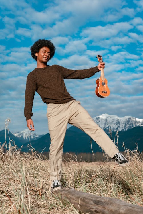 Man in Outfit of Natural Colors Holding Ukulele and Walking Outdoors