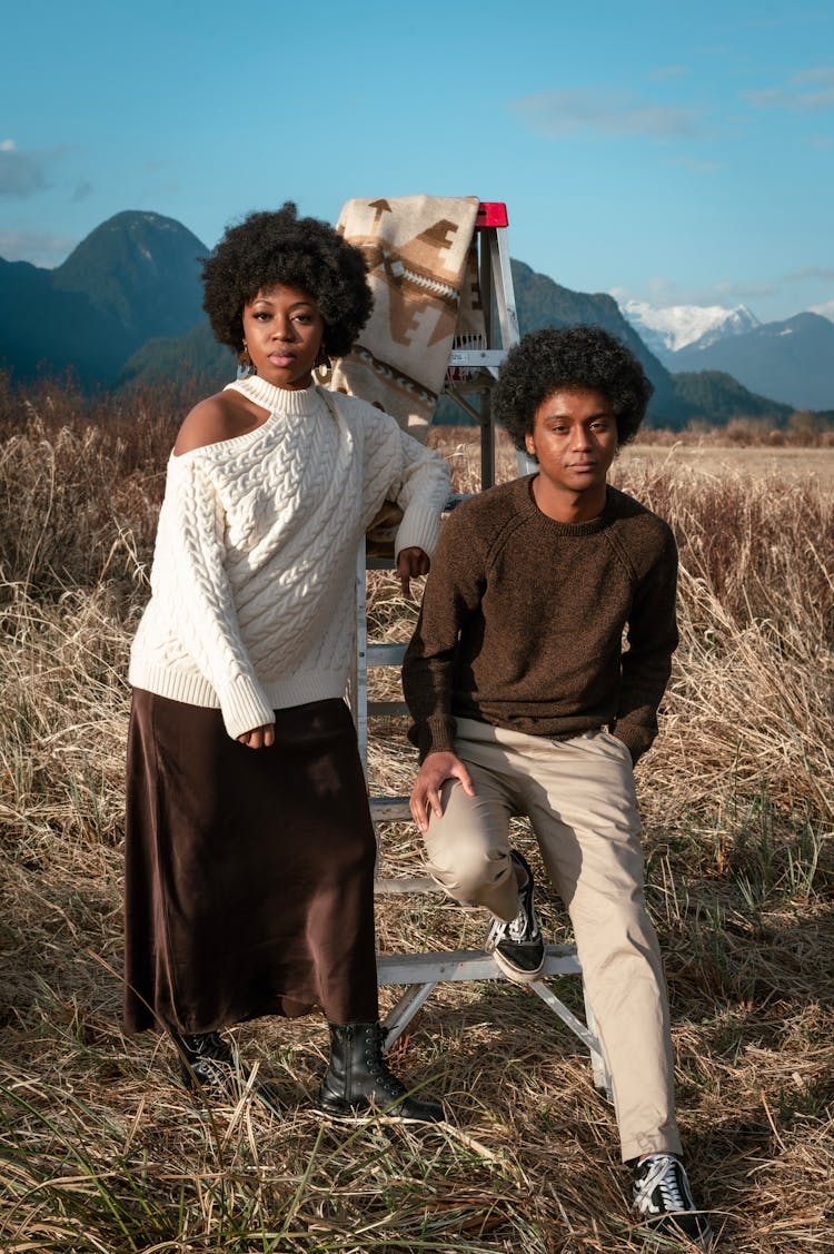 A Woman In White Sweater Standing Near The Man Sitting On The Ladder