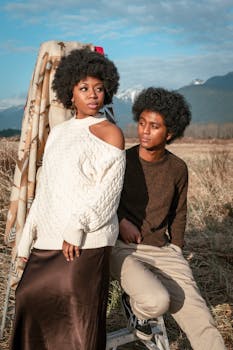 Stylish couple with afro hairstyles posing in a rustic field against a mountain backdrop.
