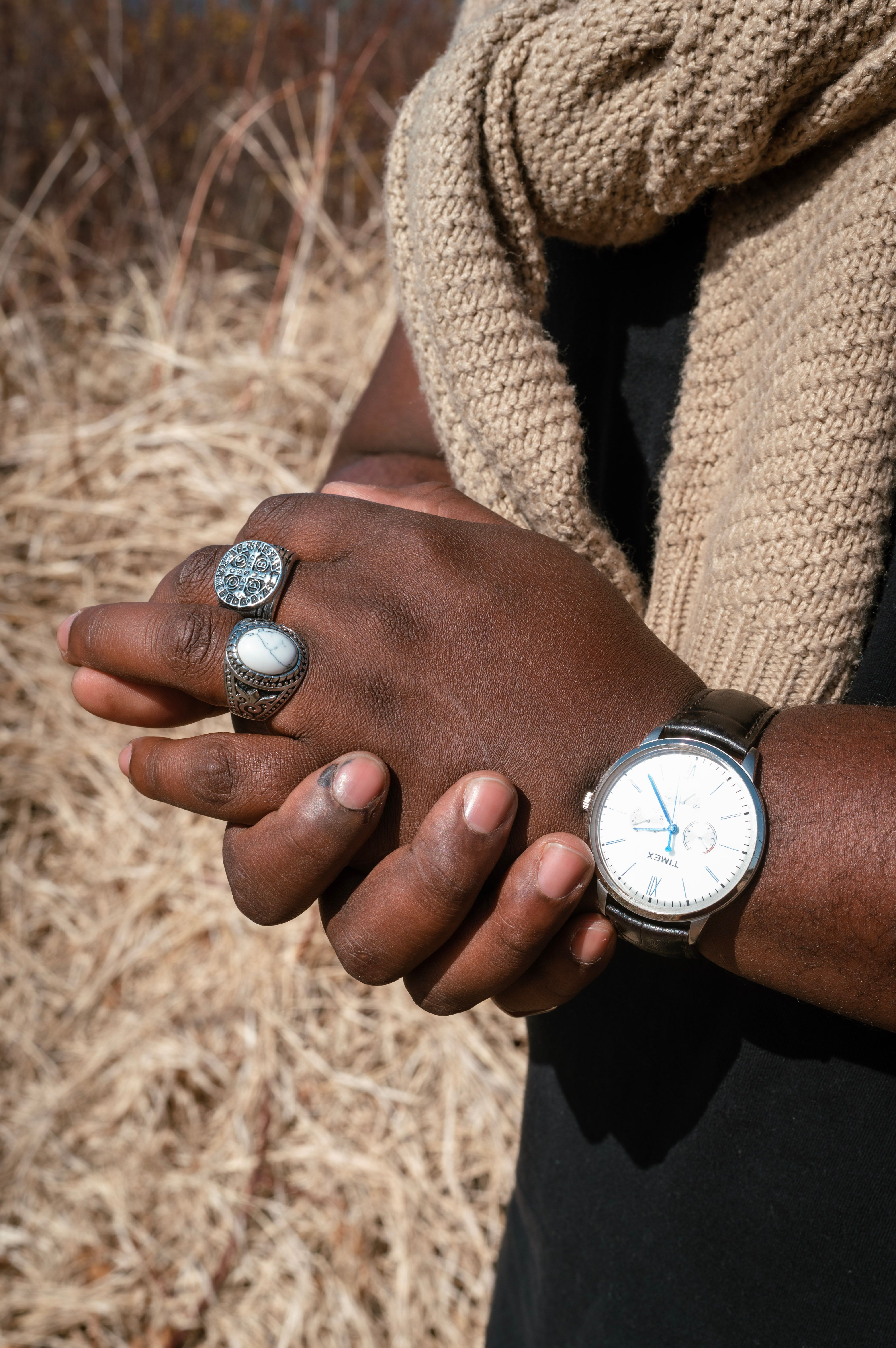Close-up of hands in black shirt adorned with rings, watch, and a knitted scarf.