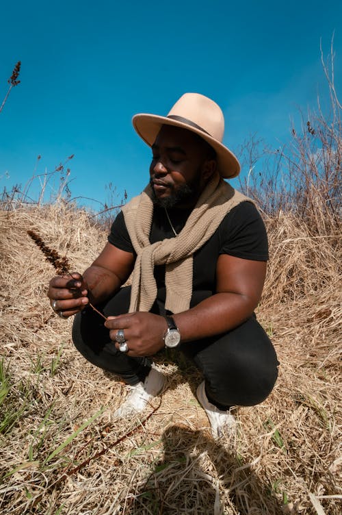 Man in Brown Hat and Brown Scarf Sitting on Brown Grass Field