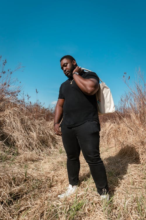 бесплатная Мужчина в черной футболке и черных штанах стоит на поле коричневой травы Стоковое фото