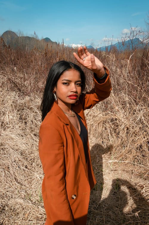 Woman in Orange Coat Standing on Brown Grass Field